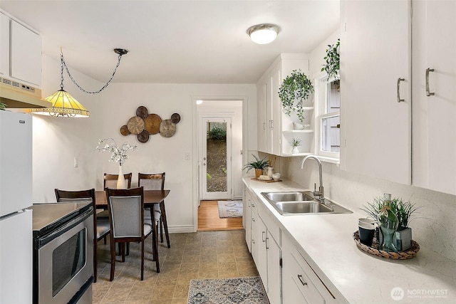 kitchen with a sink, under cabinet range hood, white cabinetry, freestanding refrigerator, and light countertops