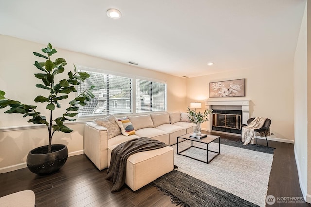 living room with dark wood-style floors, visible vents, baseboards, and a glass covered fireplace