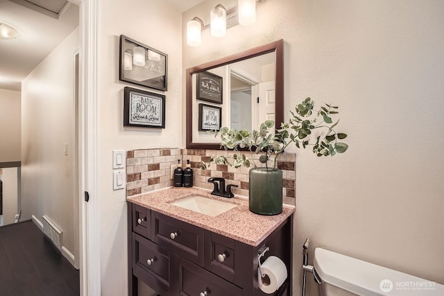 half bathroom featuring visible vents, toilet, backsplash, wood finished floors, and vanity