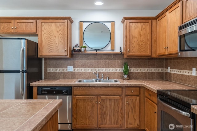 kitchen with a sink, stainless steel appliances, brown cabinetry, decorative backsplash, and tile counters