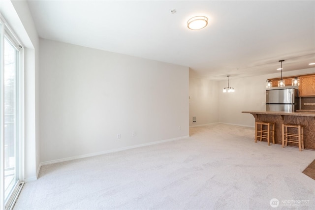 unfurnished living room featuring baseboards, light carpet, and a notable chandelier