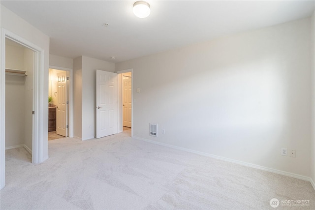 unfurnished bedroom featuring a spacious closet, baseboards, visible vents, and light carpet