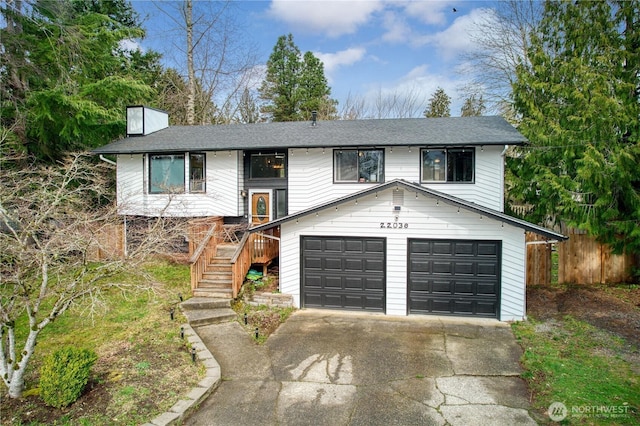 bi-level home featuring a chimney, fence, concrete driveway, an attached garage, and stairs