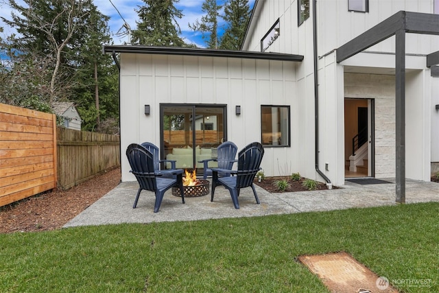 rear view of house featuring board and batten siding, fence, an outdoor fire pit, a lawn, and a patio area