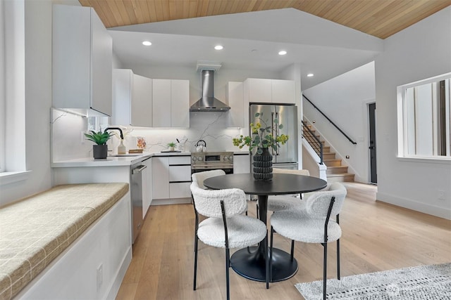 kitchen with wall chimney range hood, lofted ceiling, white cabinets, stainless steel appliances, and modern cabinets