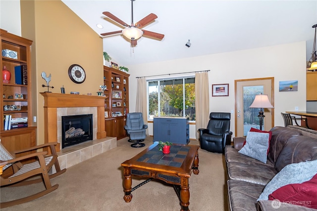 carpeted living area with a tiled fireplace, a ceiling fan, and high vaulted ceiling