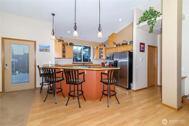 kitchen with a kitchen breakfast bar, stainless steel appliances, a peninsula, light wood finished floors, and glass insert cabinets