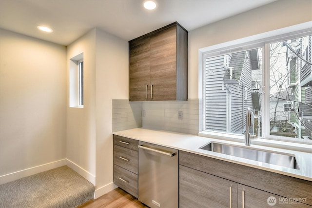 kitchen with a sink, backsplash, light countertops, baseboards, and dishwasher