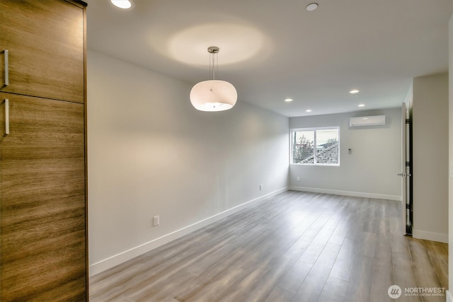 empty room with recessed lighting, wood finished floors, baseboards, and a wall mounted AC