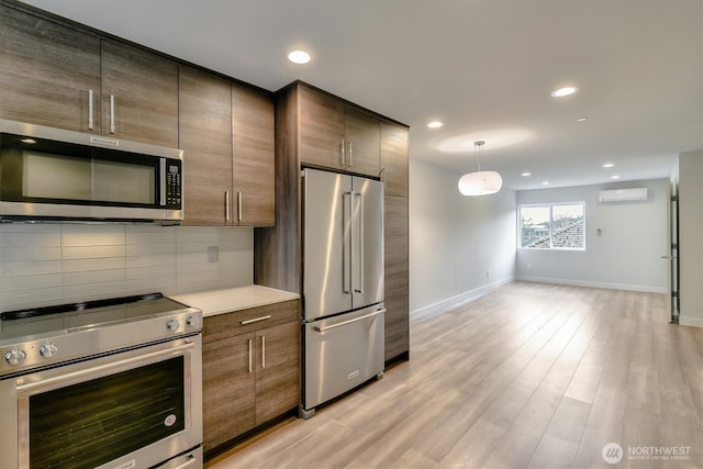 kitchen with baseboards, a wall mounted AC, light wood-style flooring, decorative backsplash, and appliances with stainless steel finishes