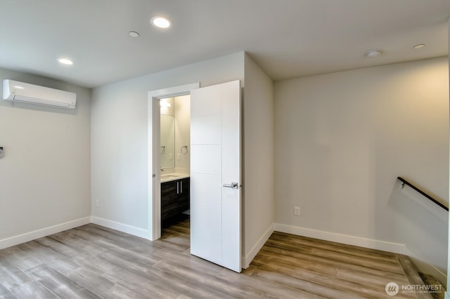 interior space with recessed lighting, light wood-style flooring, a wall mounted AC, and baseboards