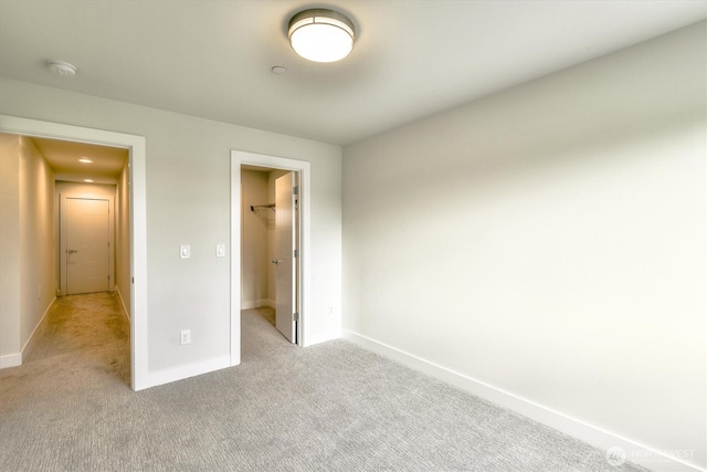 unfurnished bedroom with baseboards, light carpet, a closet, and a walk in closet