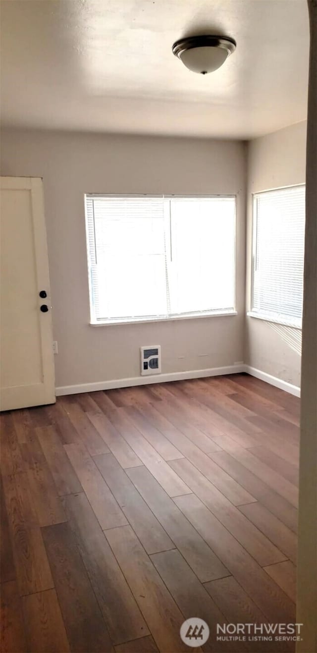 empty room featuring plenty of natural light, dark wood-style floors, and baseboards