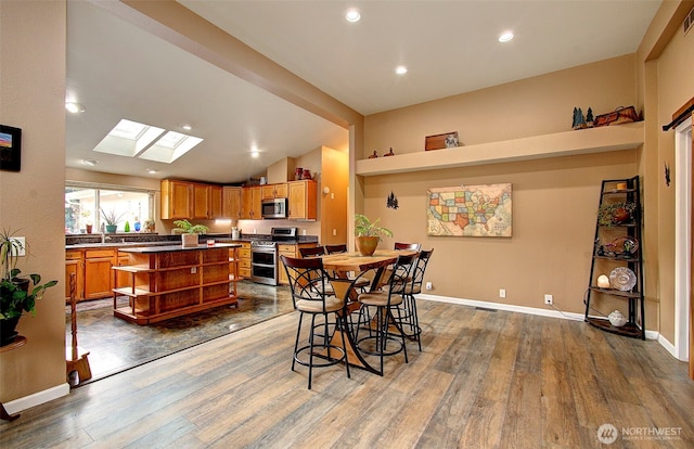 dining room featuring lofted ceiling with skylight, recessed lighting, wood finished floors, and baseboards