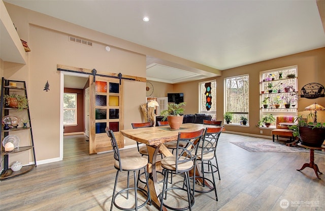 dining space featuring light wood finished floors, visible vents, baseboards, and a barn door