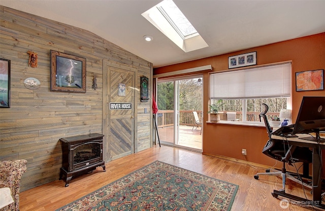 office space with vaulted ceiling with skylight, wooden walls, wood finished floors, and a wood stove