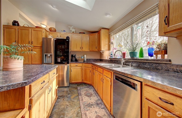 kitchen featuring lofted ceiling with skylight, dark countertops, appliances with stainless steel finishes, and a sink