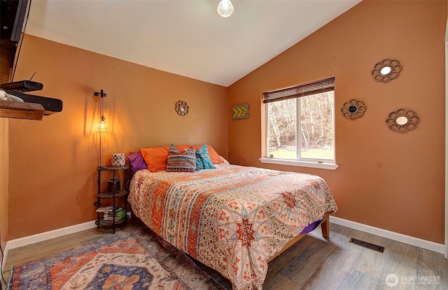 bedroom featuring visible vents, baseboards, lofted ceiling, and wood finished floors