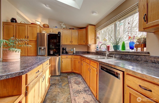 kitchen featuring lofted ceiling with skylight, appliances with stainless steel finishes, dark countertops, and a sink