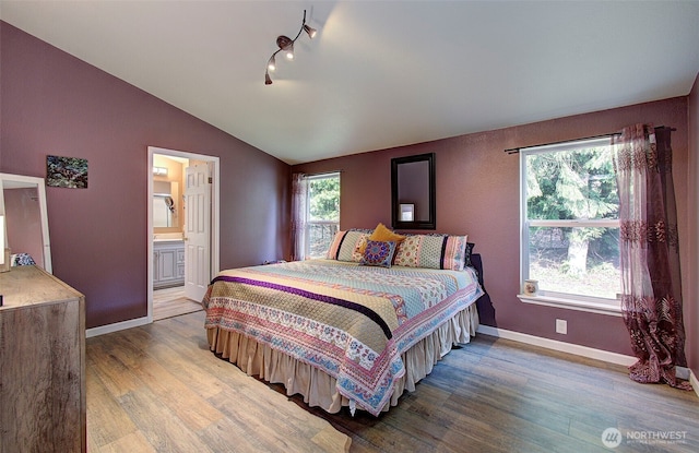 bedroom featuring connected bathroom, baseboards, wood finished floors, and vaulted ceiling