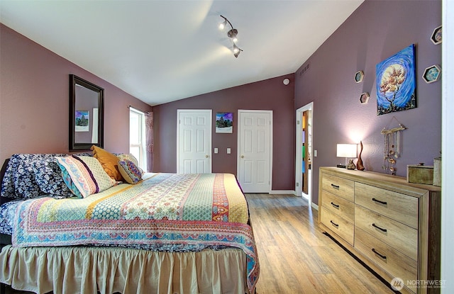 bedroom with light wood finished floors, track lighting, baseboards, and lofted ceiling