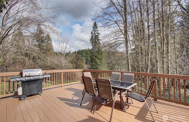 deck featuring a grill, outdoor dining space, and a wooded view