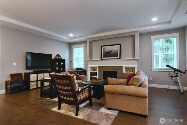 living room with a raised ceiling, wood finished floors, baseboards, and a tile fireplace