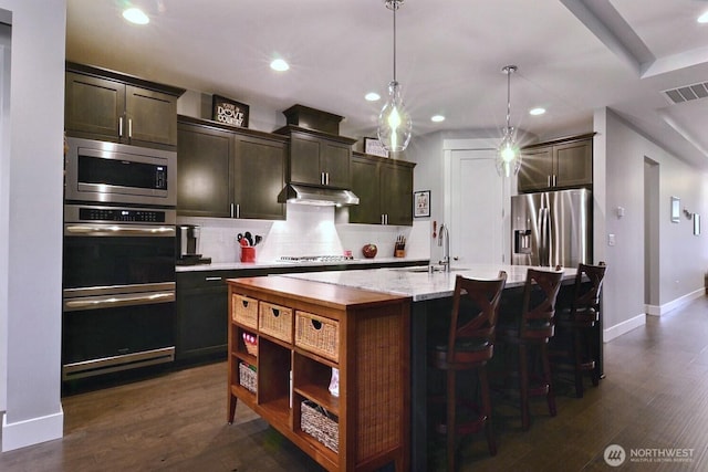 kitchen featuring visible vents, an island with sink, stainless steel appliances, decorative backsplash, and under cabinet range hood