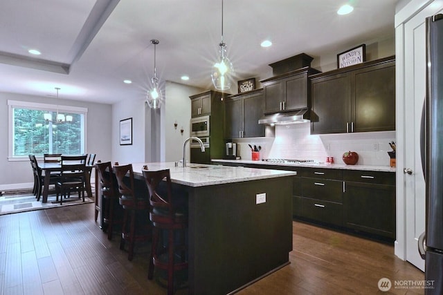 kitchen with dark wood finished floors, stainless steel appliances, under cabinet range hood, and a sink