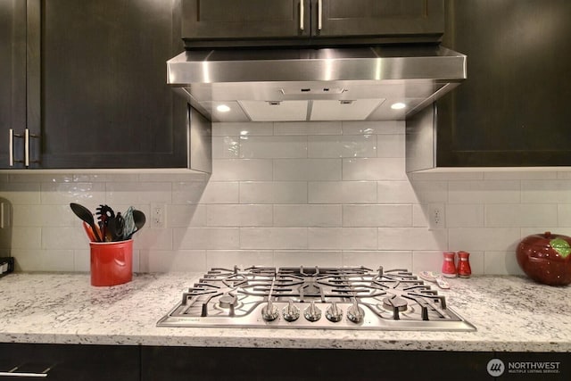 kitchen with light stone counters, wall chimney exhaust hood, tasteful backsplash, and stainless steel gas cooktop