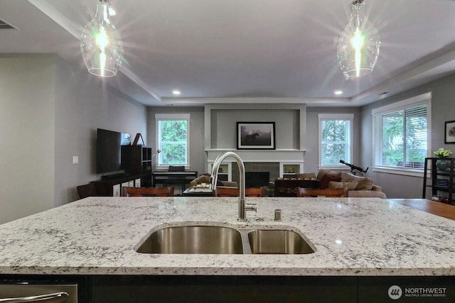 kitchen with a healthy amount of sunlight, light stone countertops, open floor plan, a fireplace, and a sink