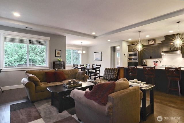 living room with a notable chandelier, a raised ceiling, dark wood finished floors, recessed lighting, and baseboards