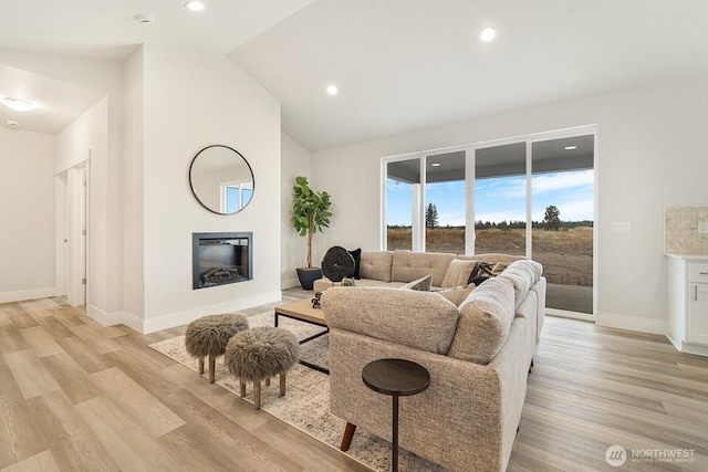 living room with baseboards, high vaulted ceiling, recessed lighting, light wood-style floors, and a glass covered fireplace