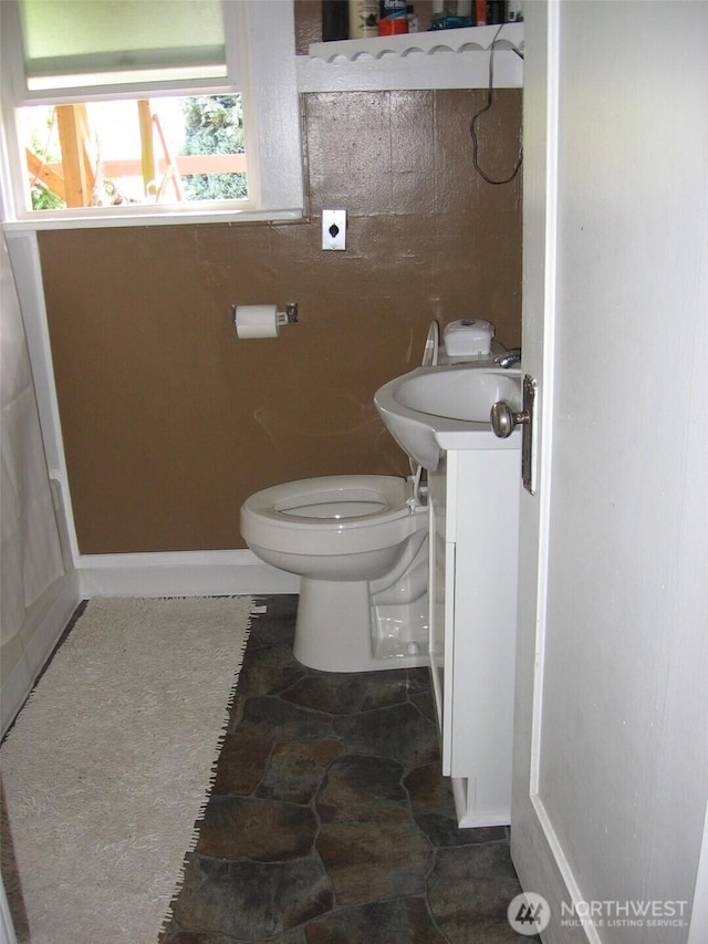 half bathroom with baseboards, toilet, and vanity