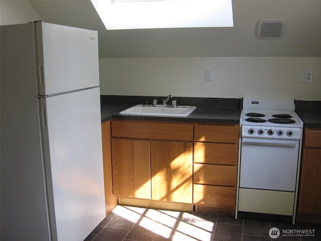 kitchen featuring dark countertops, dark tile patterned floors, brown cabinetry, white appliances, and a sink