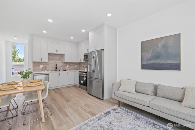 kitchen featuring appliances with stainless steel finishes, white cabinets, light wood finished floors, decorative backsplash, and light countertops