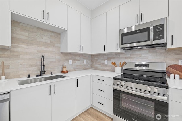 kitchen with tasteful backsplash, light wood finished floors, light countertops, appliances with stainless steel finishes, and a sink