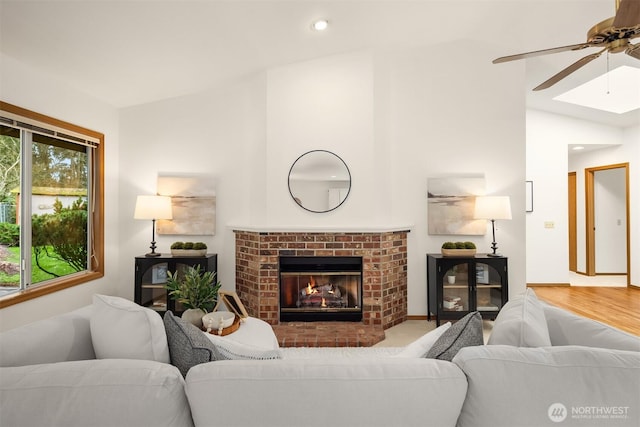 living area with a brick fireplace, baseboards, recessed lighting, vaulted ceiling with skylight, and a ceiling fan