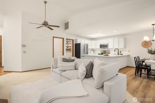 living room with light wood finished floors, visible vents, baseboards, lofted ceiling, and ceiling fan with notable chandelier