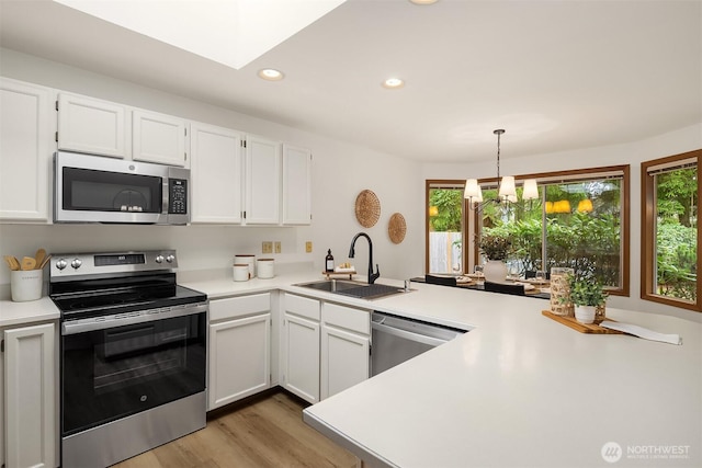 kitchen featuring a sink, appliances with stainless steel finishes, a peninsula, white cabinets, and light countertops