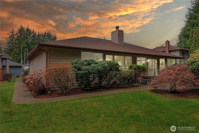 back of property at dusk featuring a lawn, roof with shingles, and a chimney