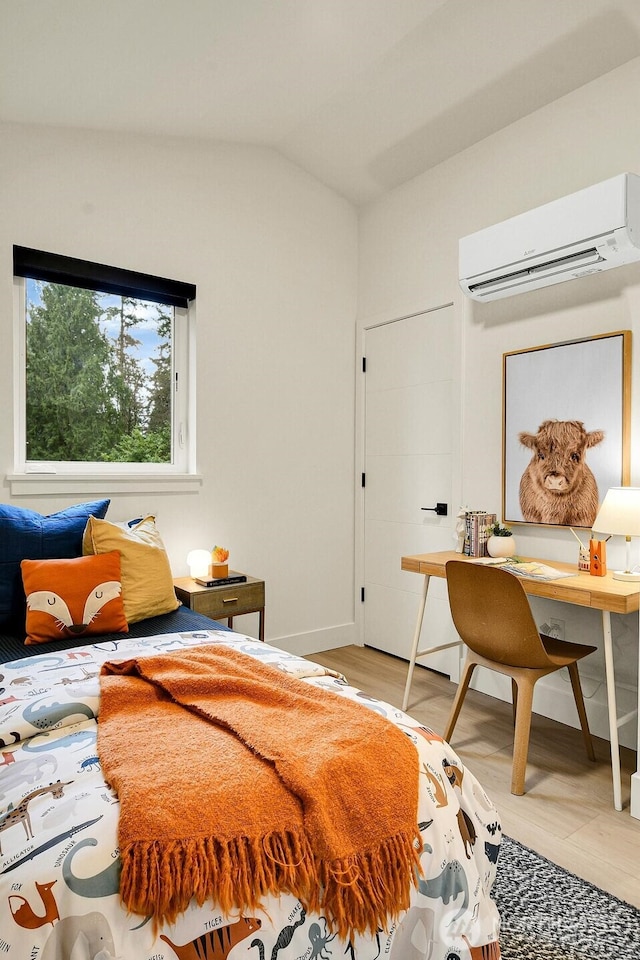 bedroom featuring light wood finished floors, baseboards, a wall mounted AC, and lofted ceiling