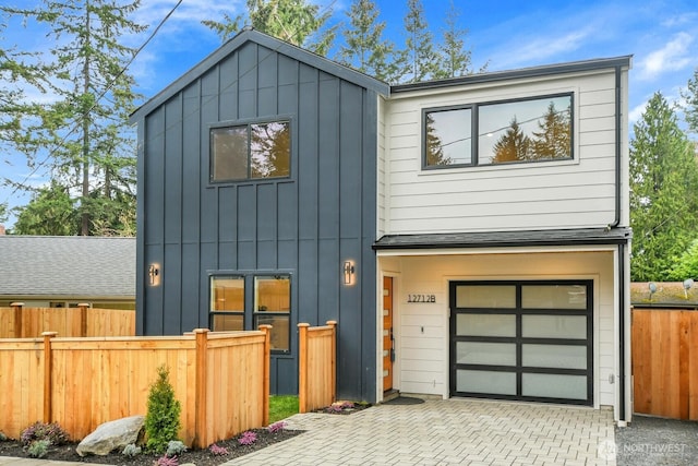 modern home with board and batten siding, decorative driveway, a garage, and fence