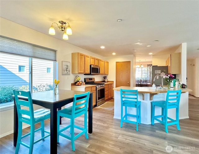 kitchen featuring a peninsula, light wood-style floors, appliances with stainless steel finishes, a kitchen breakfast bar, and a notable chandelier