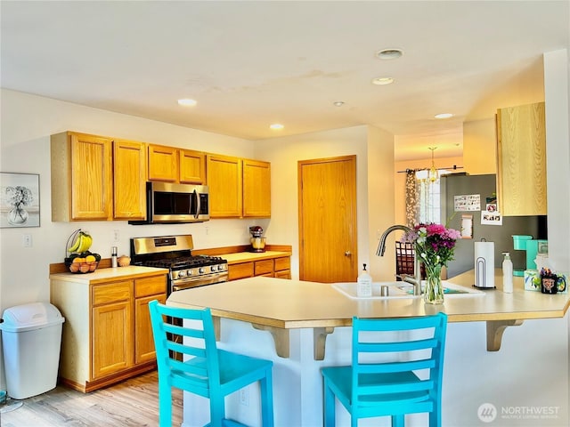 kitchen featuring a breakfast bar, a sink, stainless steel appliances, a peninsula, and light countertops