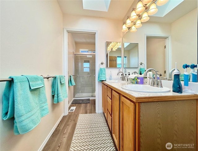 full bathroom with visible vents, a stall shower, a sink, wood finished floors, and a skylight