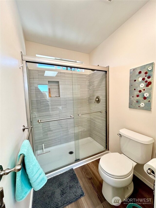 bathroom with toilet, wood finished floors, and a stall shower