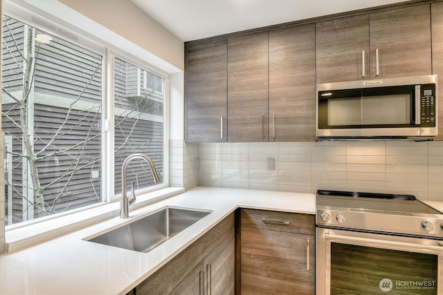 kitchen featuring a sink, decorative backsplash, light countertops, stainless steel appliances, and modern cabinets