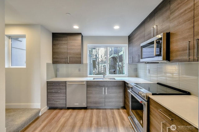 kitchen featuring light wood finished floors, a sink, backsplash, stainless steel appliances, and light countertops