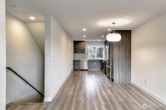 kitchen featuring dark brown cabinetry, light wood-type flooring, light countertops, appliances with stainless steel finishes, and modern cabinets